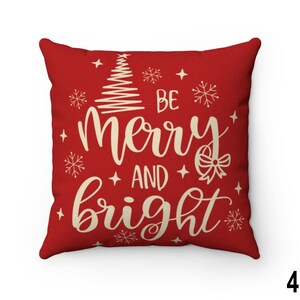 Pu&ograve; includere: Un cuscino quadrato rosso con la scritta "BE merry AND bright" in crema. Il cuscino presenta un albero di Natale, fiocchi di neve e stelle, perfetto per le feste.