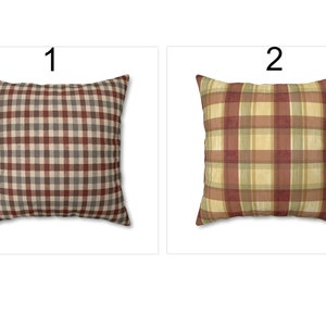 May include: Two square throw pillows with plaid patterns. Pillow 1 features a brown, gray, and beige checkered design. Pillow 2 displays a plaid pattern in shades of red, yellow, and green. Both pillows are on a white background.