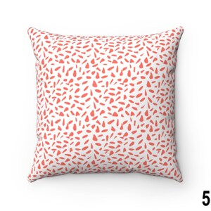 May include: A white cushion with a coral pink abstract pattern. The pattern is made up of small, irregular shapes.