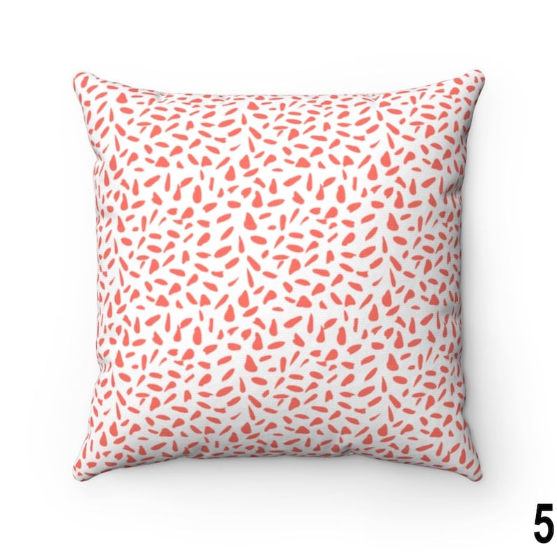 May include: A white cushion with a coral pink abstract pattern. The pattern is made up of small, irregular shapes.