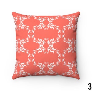 May include: A coral-coloured throw pillow with a white floral pattern. The pillow is square shaped and has a soft, plush texture.