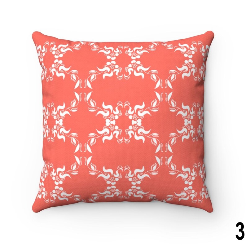 May include: A coral-coloured throw pillow with a white floral pattern. The pillow is square shaped and has a soft, plush texture.