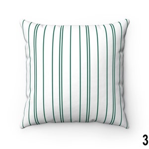 May include: A white throw pillow with dark green vertical stripes. The pillow is a square shape and has a white background.