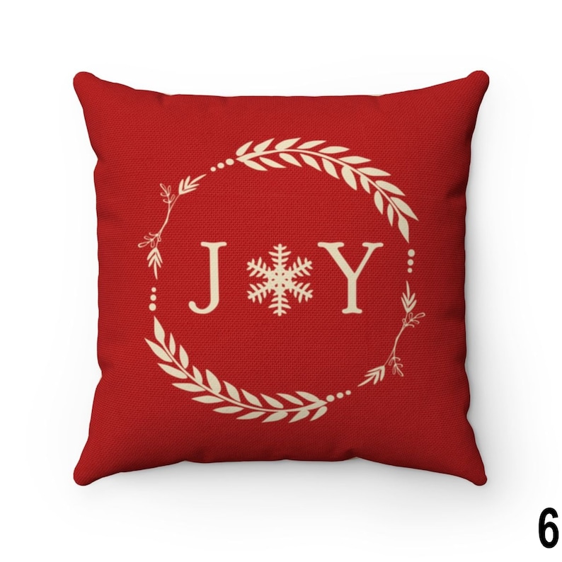 Pu&ograve; includere: Un cuscino decorativo rosso quadrato con la scritta "JOY" in bianco, con un fiocco di neve tra le lettere. Le lettere sono all'interno di una ghirlanda color crema con foglie e bacche. Un accento festivo per le festivit&agrave;.