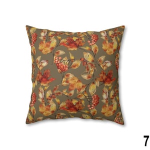 May include: Square throw pillow with a repeating pattern of autumn leaves and berries in shades of orange, red, and yellow on a muted olive green background. The pillow is a decorative accent for a living room or bedroom.