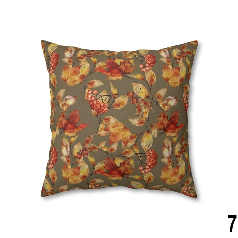 May include: Square throw pillow with a repeating pattern of autumn leaves and berries in shades of orange, red, and yellow on a muted olive green background. The pillow is a decorative accent for a living room or bedroom.
