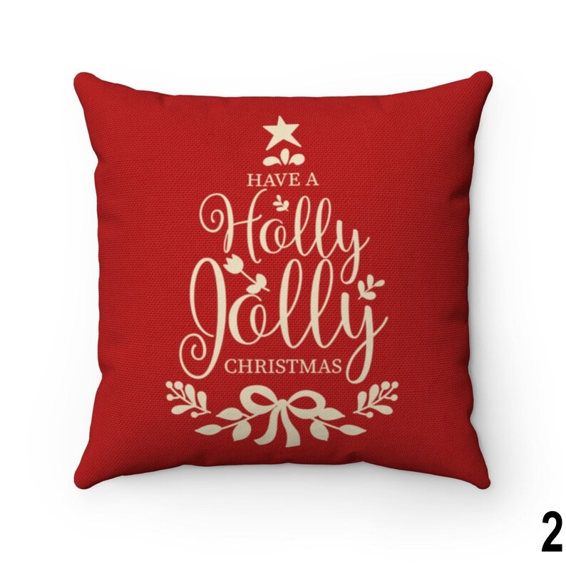 Pu&ograve; includere: Un cuscino quadrato rosso con la scritta "Have a Holly Jolly Christmas" in crema in un carattere decorativo. Il testo &egrave; disposto a forma di albero di Natale, con una stella in cima e un fiocco in basso.