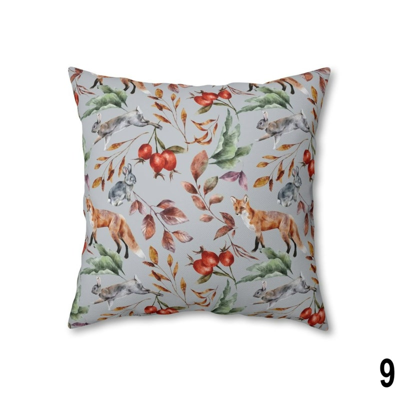 May include: Square throw pillow with a repeating pattern of foxes, rabbits, berries, and leaves in shades of orange, brown, green, and gray. The pillow has a light gray background and is a square shape.