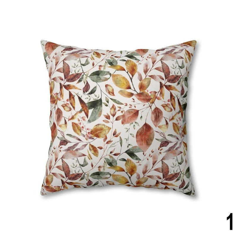 May include: Square throw pillow with a botanical leaf pattern. The pillow features a white background with a repeating design of autumn leaves in shades of brown, green, and yellow. The leaves are detailed with watercolor-style shading.