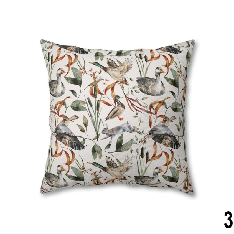 May include: Square throw pillow with a nature-themed pattern. The design features ducks, geese, and a rabbit amidst foliage in shades of green, brown, and beige. The pillow has a white background.