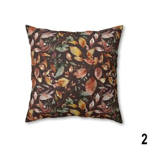 May include: Square throw pillow with a dark brown background and a repeating pattern of autumn leaves in shades of orange, yellow, and green. The leaves are detailed and create a natural, seasonal theme. The pillow is a decorative home accent.
