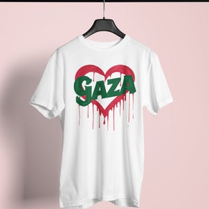 以下が含まれることがあります： 赤いハートと緑色の文字で「GAZA」と書かれた白いTシャツ。赤い塗料が垂れている。