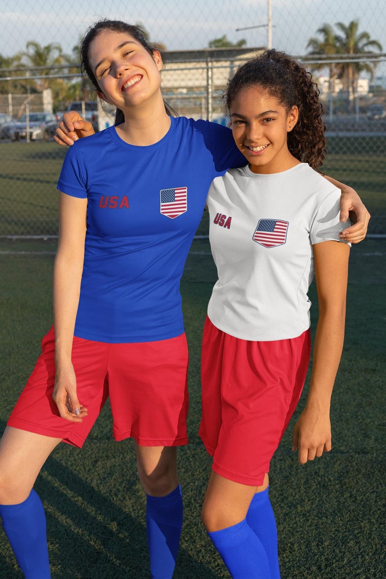 Peut inclure: Deux personnes portant des tenues de sport assorties. L'une porte un t-shirt bleu et l'autre un t-shirt blanc, tous deux avec le mot "USA" et un &eacute;cusson du drapeau am&eacute;ricain. Elles portent &eacute;galement des shorts rouges et des chaussettes bleues.
