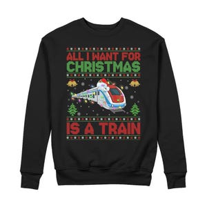 Könnte beinhalten: Ein schwarzes Langarm-Sweatshirt mit einem Grafikdruck eines Zuges, der eine Weihnachtsmütze trägt und mit bunten Lichterketten geschmückt ist. Der Text lautet ALL I WANT FOR CHRISTMAS IS A TRAIN, umrahmt von roten, grünen und weißen Mustern.