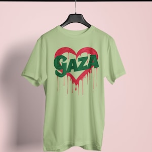 以下が含まれることがあります： 薄い緑色のTシャツに、赤いハートの中に緑色の文字で「GAZA」と書かれています。ハートは赤い塗料が垂れています。