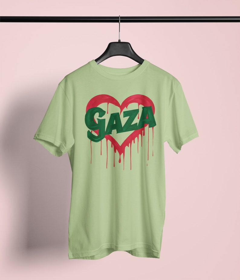 以下が含まれることがあります： 薄い緑色のTシャツに、赤いハートの中に緑色の文字で「GAZA」と書かれています。ハートは赤い塗料が垂れています。