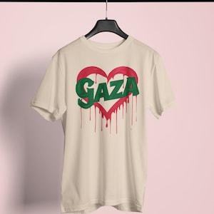 以下が含まれることがあります： ベージュのTシャツに、赤いハートの中に緑色の文字で「GAZA」と書かれている。ハートは赤い塗料が垂れている。