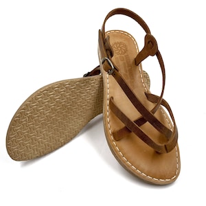 May include: Brown leather sandals with criss-cross straps and a buckle closure. The sandals have a flat sole and are made of genuine leather.