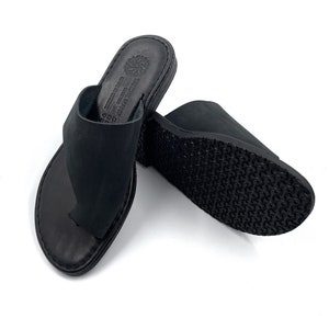 Op de afbeelding: Een paar zwarte leren sandalen met een eenvoudig ontwerp. De sandalen hebben een gesloten teen en een dikke, textuurrijke zool.