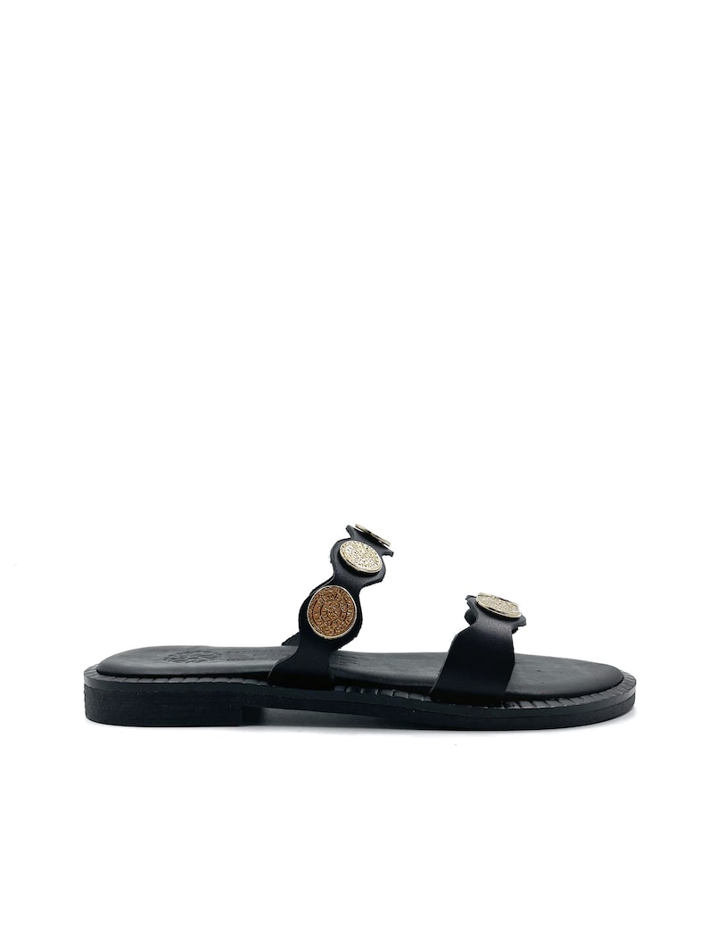 May include: Black leather sandals with gold and brown coin accents. The sandals have two straps and a flat sole.