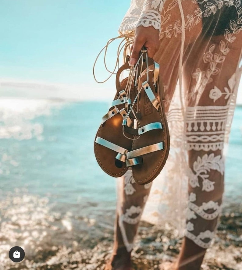 May include: A pair of brown leather sandals with silver straps. The sandals are tied together with a gold cord.