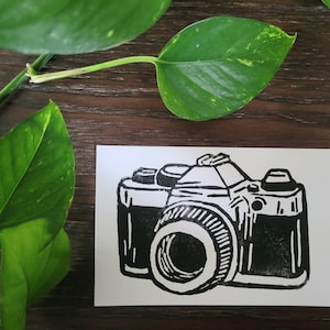 Peut inclure: Illustration en noir et blanc d'un appareil photo vintage avec un grand objectif. L'appareil photo est dessiné dans un style simple et bloc.