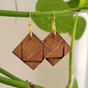 May include: A pair of wooden earrings with a geometric diamond shape. The earrings are made of dark brown wood and have gold hooks.