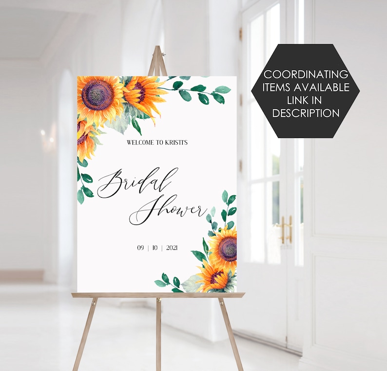 May include: A white welcome sign with a sunflower and greenery design. The text reads "Welcome to Kristi's Bridal Shower 09 | 10 | 2021".