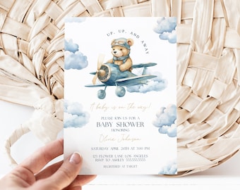 May include: A baby shower invitation with a blue and white watercolor design. A teddy bear wearing a pilot's hat and goggles is flying a blue airplane in the clouds. The text reads "Up, Up, and Away! It baby is on the way!"  Please join us for a baby shower honoring Olivia Johnson. Saturday, April 24th at 3:00 PM. 123 Flower Lane Los Angeles. RSVP to Ashley 555-555-5555. Registered at Target.