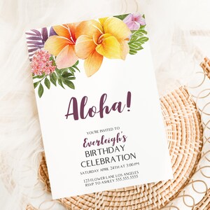 May include: White invitation card with the word "Aloha!" in purple script, adorned with watercolor flowers. The card announces a birthday celebration with details. The card is placed on a woven mat.