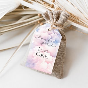 May include: A small burlap bag with a white tag attached. The tag has a watercolor design of pink and blue clouds with the text "thank you" and "Love, Carrie".