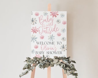 May include: A white sign with pink and blue snowflakes and the text "Baby it's cold outside" and "Welcome to Olivia's Baby Shower".