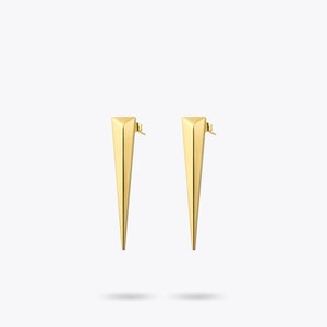 May include: A pair of gold-toned earrings with a triangular shape. The earrings have a pointed tip and a small post for insertion.