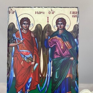 May include: A religious icon depicting two figures with halos, wings, and robes. One figure holds a sword, the other a staff. The figures are set against a background with text in a foreign language. The color palette includes red, blue, green, and gold.