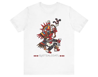Puede incluir: Una camiseta blanca de manga corta con un gráfico colorido de la deidad Quetzalcoatl en tonos rojo, azul y amarillo. La figura lleva un tocado elaborado y sostiene un bastón. El texto QVETZALCOATL está impreso debajo en letras rojas.