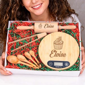 Könnte beinhalten: Ein hölzernes Backgeschenkset mit Nudelholz, Schneidebrett, Löffeln und Zangen. Das Schneidebrett und die Nudelrolle sind mit einem Cupcake-Design und dem Namen "Eloise" graviert. Das Set enthält eine digitale Küchenwaage.