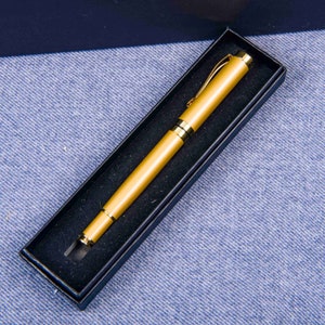 Puede incluir: Un bol&iacute;grafo de color dorado en una caja de terciopelo negro. El bol&iacute;grafo tiene un clip dorado y un capuch&oacute;n dorado.