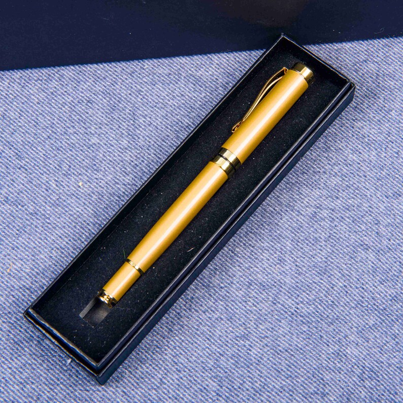 Puede incluir: Un bol&iacute;grafo de color dorado en una caja de terciopelo negro. El bol&iacute;grafo tiene un clip dorado y un capuch&oacute;n dorado.