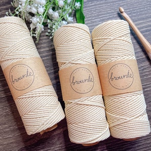 May include: Three spools of natural colored cotton rope with a brown paper label that says "brownie" on each spool. The spools are on a wooden surface.