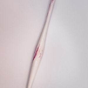 May include: White crochet hook with pink marbling. The hook has a pointed tip and a smooth handle.