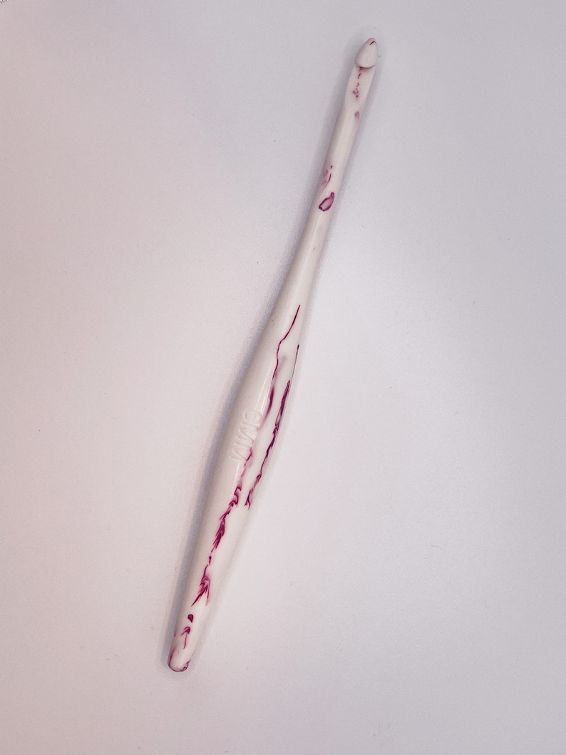 May include: White crochet hook with pink marbling. The hook is about 6 inches long.