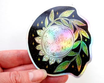 May include: A holographic sticker with a black background featuring a crescent moon surrounded by crystals and green leaves. The moon is iridescent and has a white outline. The sticker has a wavy edge.