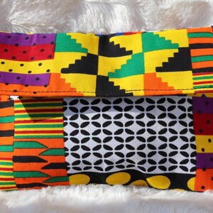 May include: A patterned fabric clutch bag with a flap closure. The design features geometric patterns and bright colours, including yellow, orange, green, and black. The clutch has a small loop on the side.