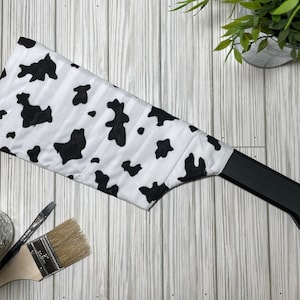 May include: A black and white cow print fabric wrapped around a black wooden hanger.
