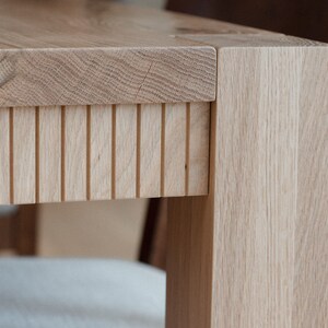 Puede incluir: Primer plano de una mesa de madera clara con un dise&ntilde;o de listones en la parte inferior de la encimera. La mesa tiene un acabado de madera natural y est&aacute; hecha de madera maciza.