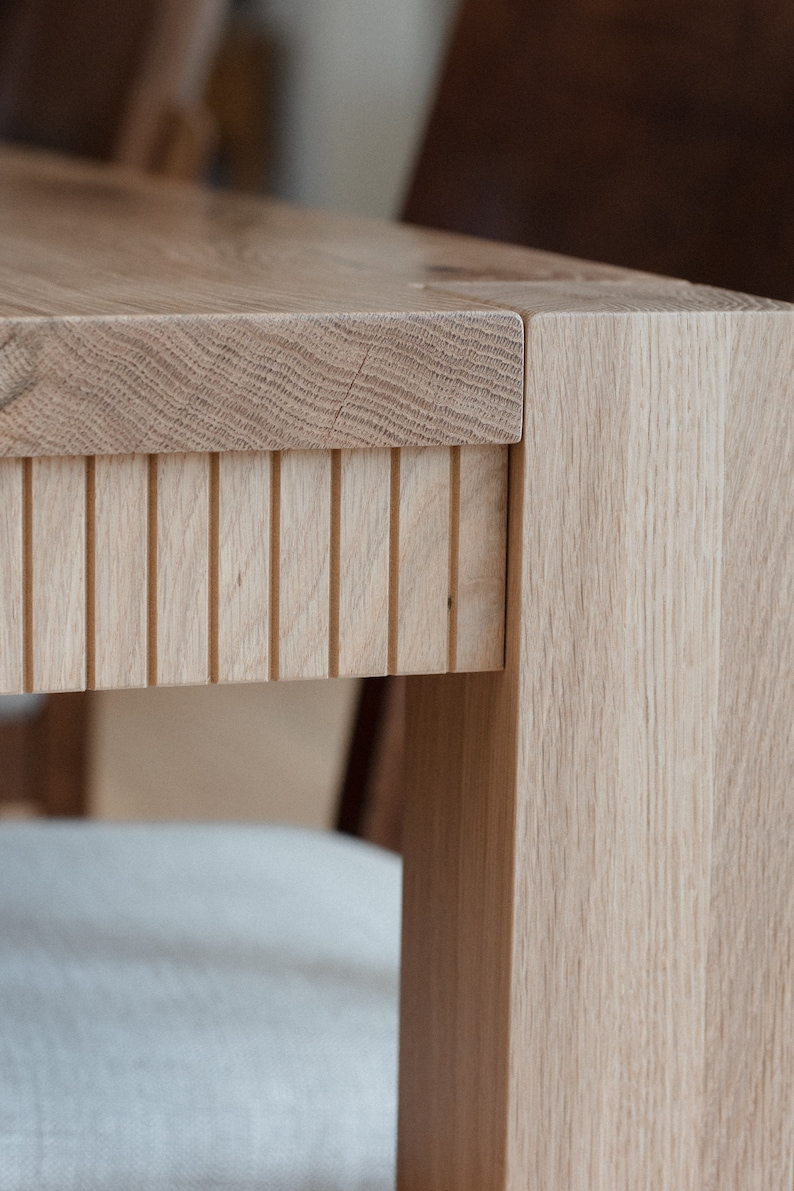 Puede incluir: Primer plano de una mesa de madera clara con un dise&ntilde;o de listones en la parte inferior de la encimera. La mesa tiene un acabado de madera natural y est&aacute; hecha de madera maciza.