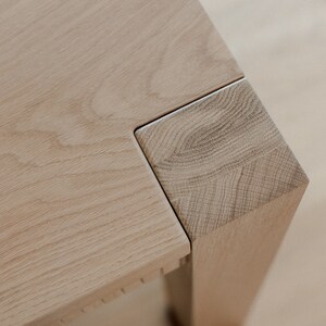 Puede incluir: Primer plano de una esquina de mesa de madera clara con una junta de inglete. La veta de la madera es visible y la superficie es lisa.