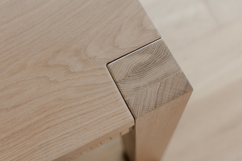 Puede incluir: Primer plano de una esquina de mesa de madera clara con una junta de inglete. La veta de la madera es visible y la superficie es lisa.