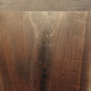 May include: A close-up of a large, dark brown wooden slab with a natural edge. The wood has a beautiful grain pattern and a smooth, polished finish.