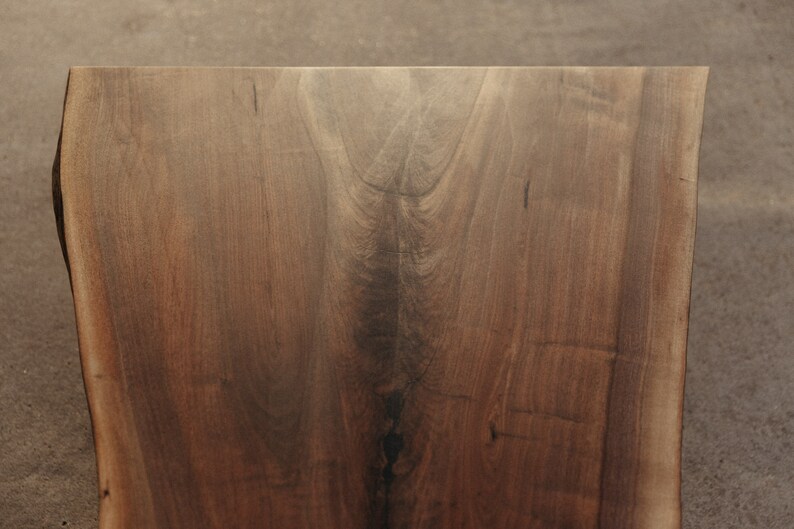 May include: A close-up of a large, dark brown wooden slab with a natural edge. The wood has a beautiful grain pattern and a smooth, polished finish.